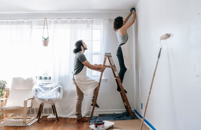 Couple renovating their home, with man supporting ladder and woman working on walls indoors. — Advantages of Online Info Soft