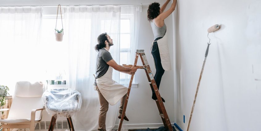 Couple renovating their home, with man supporting ladder and woman working on walls indoors. — Advantages of Online Info Soft