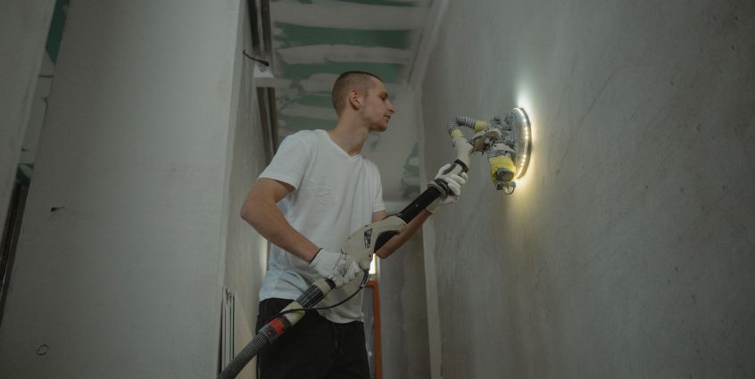 A man sanding an interior wall with an automatic sanding tool during renovation work indoors. — Ashville Park Virginia Beach:
