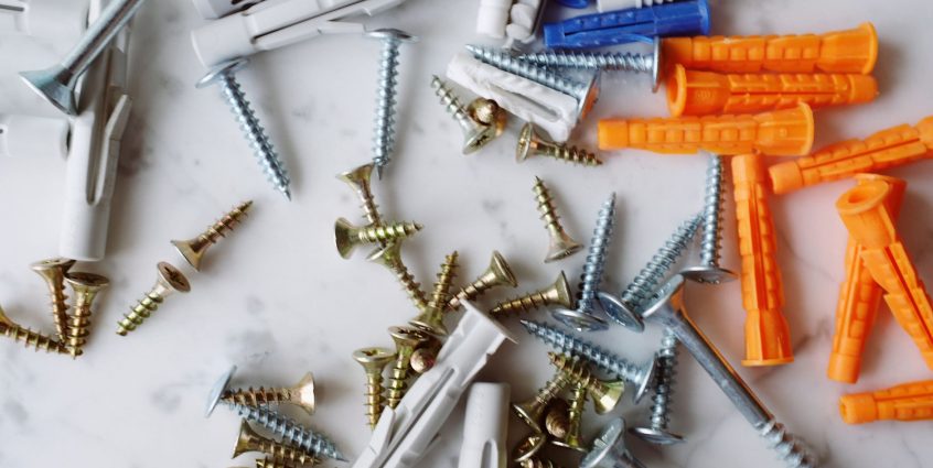 Set of various multicolored plastic dowels with metal screws of different sizes placed on white marble table in modern worksh