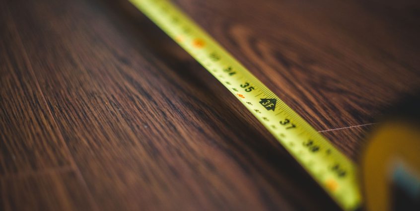 Yellow tape measure extended across a dark wooden floor, highlighting measurement details. — Backline: Judgment-Free Support