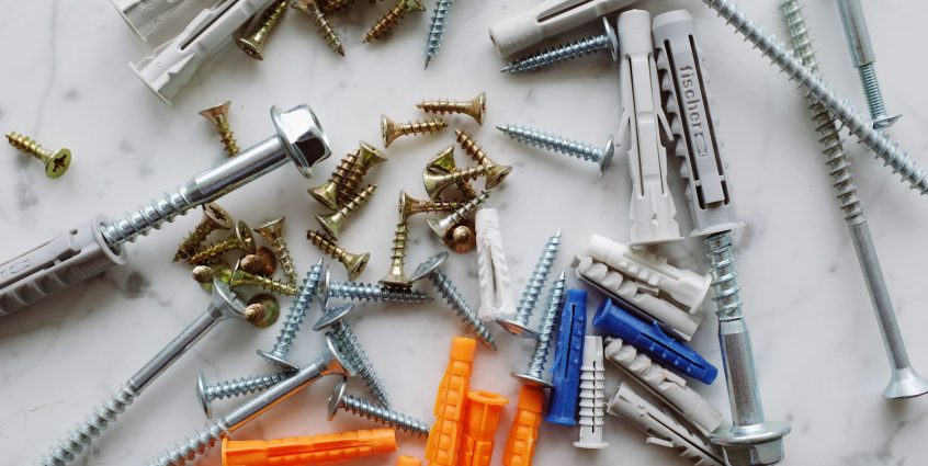 Set of assorted multicolored plastic dowels and various metal screws of different sizes placed on white marble table in works