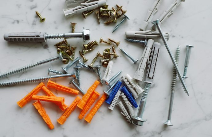 Set of various multicolored plastic dowels with metal screws of different sizes placed on white marble table in modern worksh