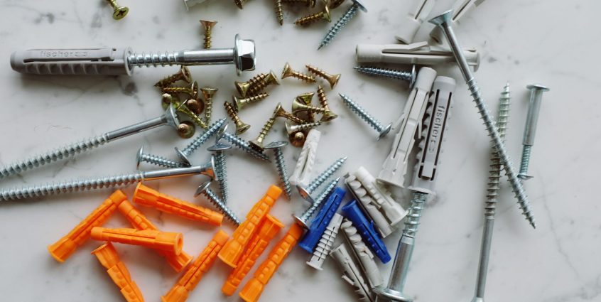 Set of various multicolored plastic dowels with metal screws of different sizes placed on white marble table in modern worksh