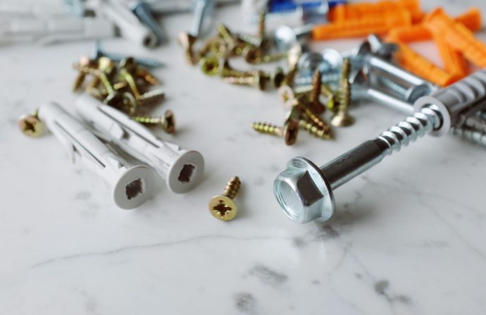 Closeup view of various multicolored plastic dowels with metal screws of different sizes placed on white marble table in mode