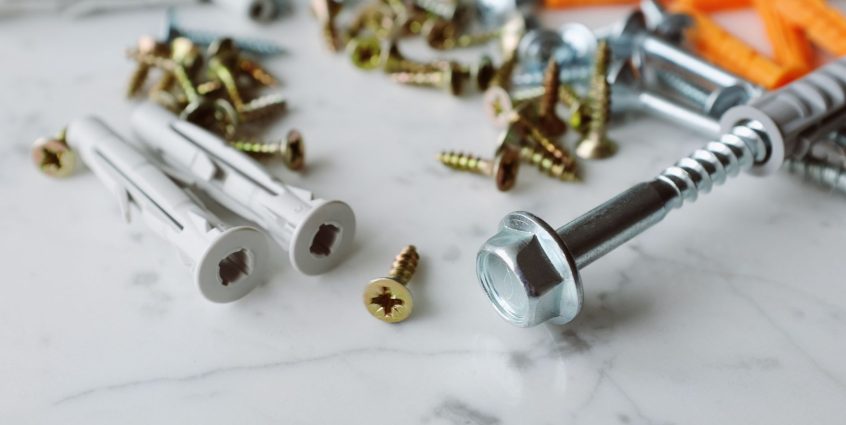 Closeup view of various multicolored plastic dowels with metal screws of different sizes placed on white marble table in mode