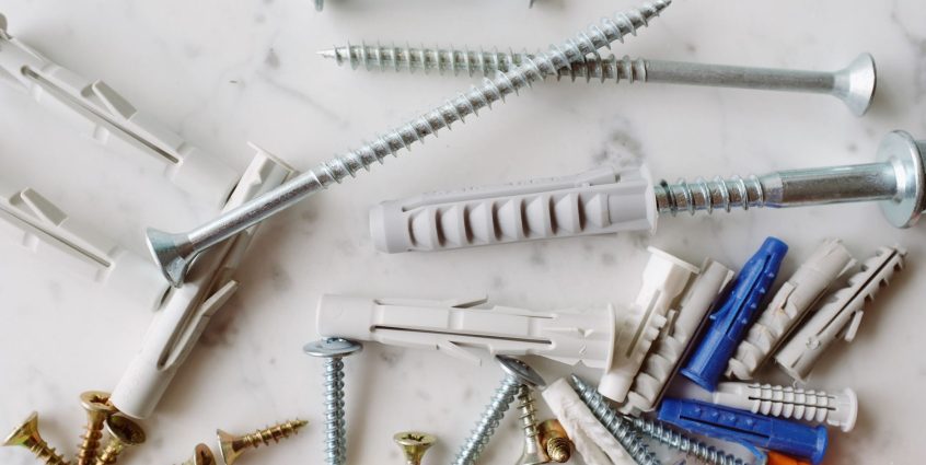 Set of various multicolored plastic dowels with metal screws of different sizes placed on white marble table in modern worksh