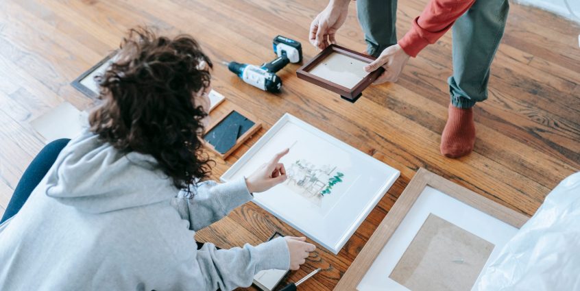 A couple organizing picture frames on a wooden floor, preparing for interior decoration or renovation. — Easy Tips To Increas