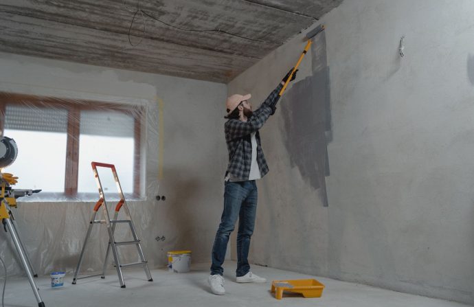 A man painting an interior wall with a roller during a home renovation project. — Essay Writing Tips