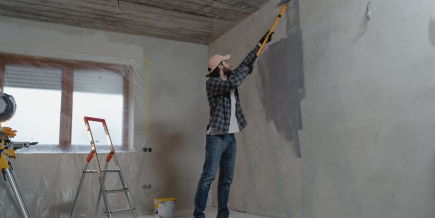 A man painting an interior wall with a roller during a home renovation project. — Essay Writing Tips