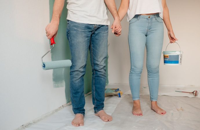 A couple engaged in home renovation, painting a wall barefoot and holding hands, symbolizing love and teamwork. — Exactly wha