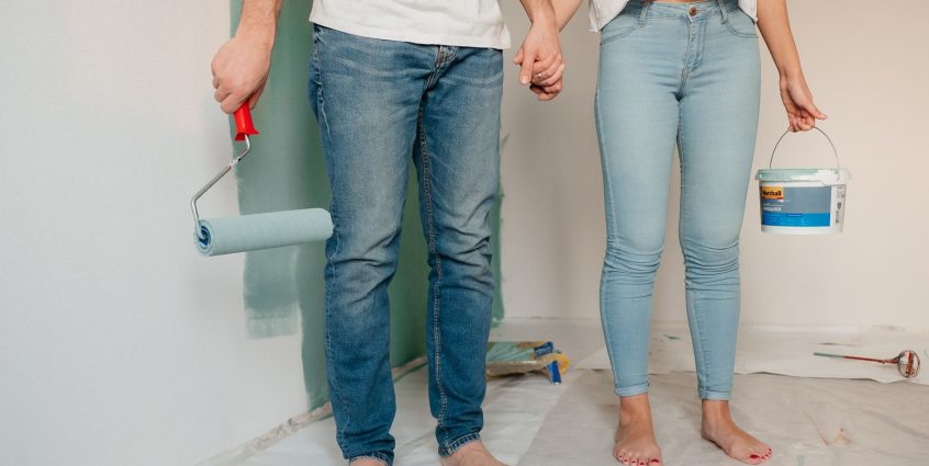 A couple engaged in home renovation, painting a wall barefoot and holding hands, symbolizing love and teamwork. — Exactly wha