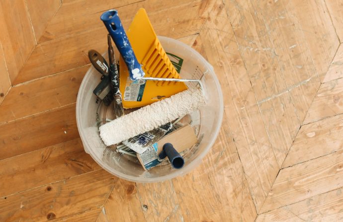 A collection of home renovation tools in a bucket on a wooden floor, ready for a painting project. — How to Buy Essays Online