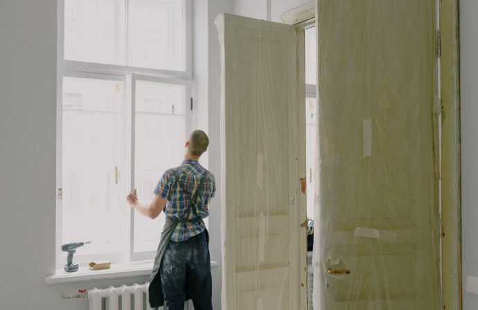Back view of unrecognizable workman in apron mounting window near drilling machine and doors in flat — How to locate Energy f