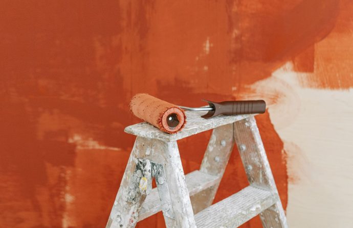 Paint roller on a ladder with a partially painted red wall in the background. — How to Write a Good Essay
