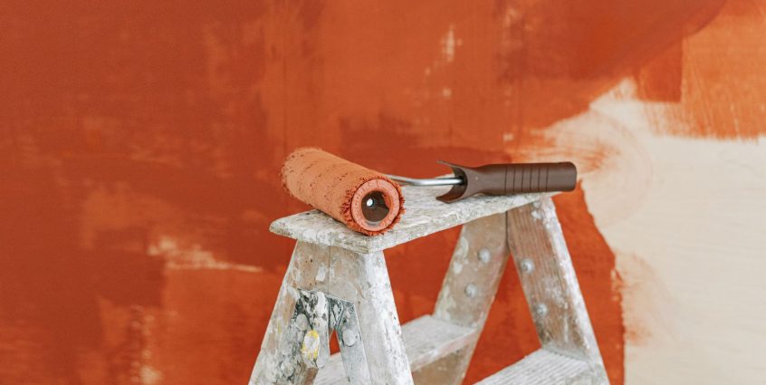 Paint roller on a ladder with a partially painted red wall in the background. — How to Write a Good Essay