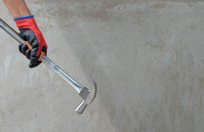 A gloved hand holding a claw hammer against a concrete wall, ideal for construction themes. — Info Room Application Developer