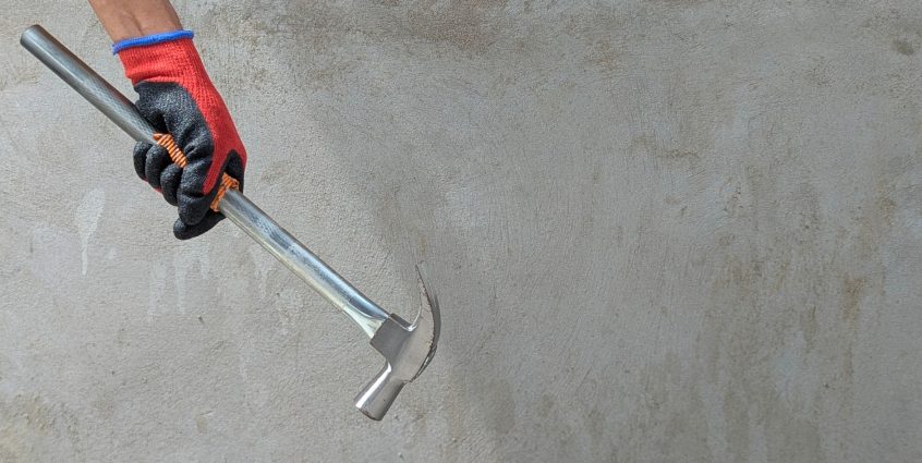 A gloved hand holding a claw hammer against a concrete wall, ideal for construction themes. — Info Room Application Developer