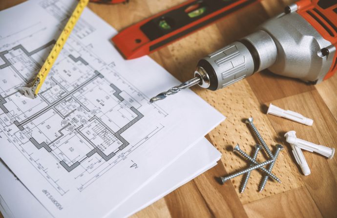 Close-up of construction blueprint with tools like drill and screws on a wooden table. — Kinds of Essay Writing