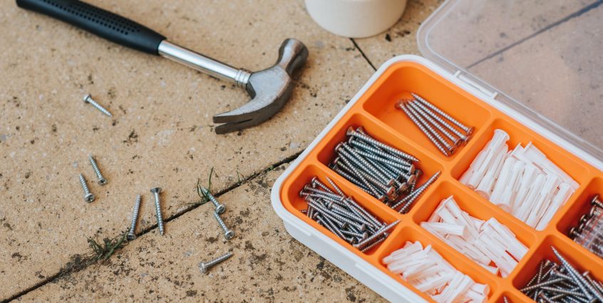 Top view of assorted repair instruments and screws in box near hammer and scotch tape on dirty tile in soft daylight — MA Ana
