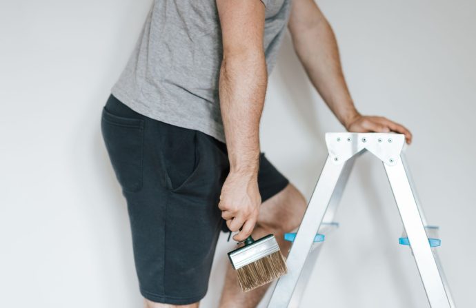 Side view of crop anonymous male decorator in casual clothes preparing to painting walls of light room while standing on step
