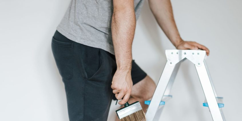 Side view of crop anonymous male decorator in casual clothes preparing to painting walls of light room while standing on step