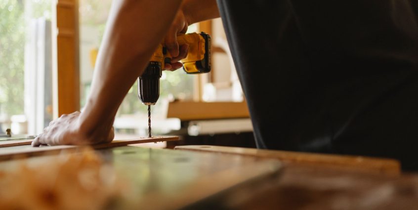 Crop anonymous male carpenter making hole on wooden plank with drill during work in studio on sunny day — Pros and cons of Ou