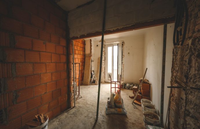 A partially renovated room with exposed brick walls and construction materials on site. — Selling Your Essay for Gain