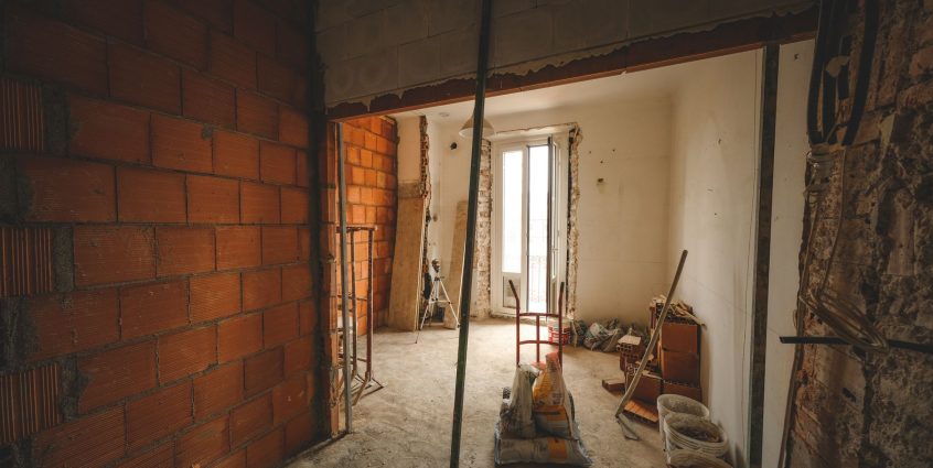 A partially renovated room with exposed brick walls and construction materials on site. — Selling Your Essay for Gain