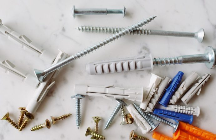 Set of various multicolored plastic dowels with metal screws of different sizes placed on white marble table in modern worksh